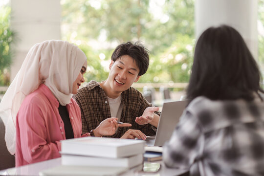 A group of diverse, multiracial young Asian university students are seen brainstorming and discussing together at a meeting. This depicts the concepts of technology and teamwork.