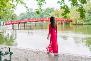 Young Asian woman tourist wearing Ao Dai (traditional Vietnamese dress) sightseeing at the Red Bridge in Hoan Kiem Lake, Hanoi, Vietnam. Copy space