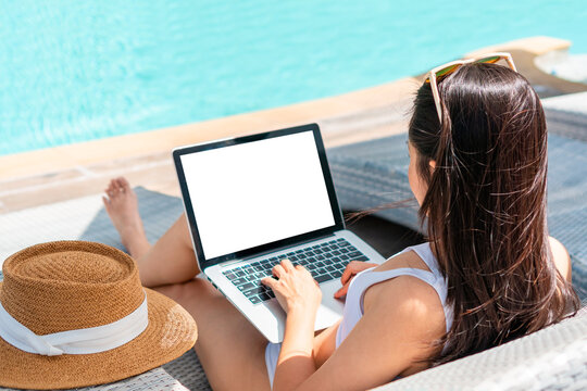Freelancer using laptop working remotely near swimming pool. Young Asian traveler woman working on computer during her summer holiday. Work from anywhere, Technology and lifestyle concept, Free space