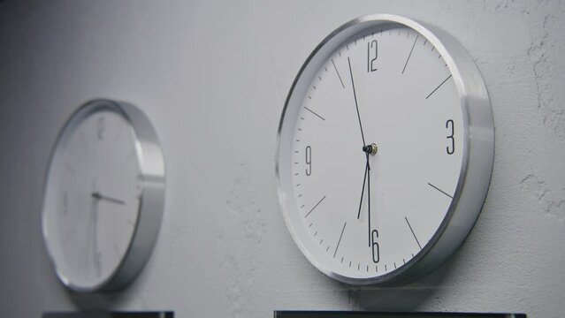 Static shot of walking wall clocks in office with modern design. Multiple white watches hang on the wall and show time of different time zones. Strict clocks with running time pointers. Close up.