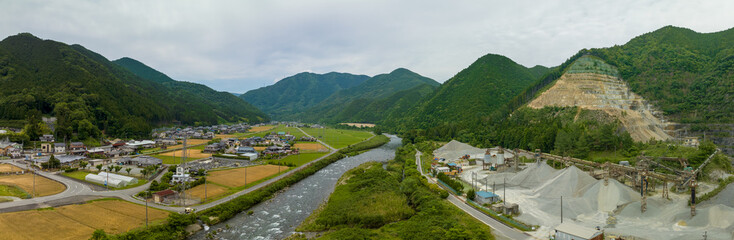 Piles of material at open pit mine by river and village in mountain landscape