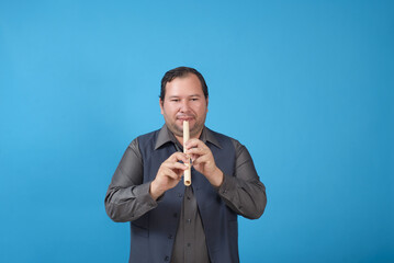 Studio portrait of a man playing a recorder. Blue background with copy space.