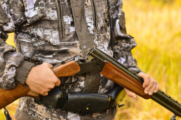 Fototapeta premium A hunter in camouflage uniform stands in the middle of an autumn meadow with a torn gun, preparing for hunting.