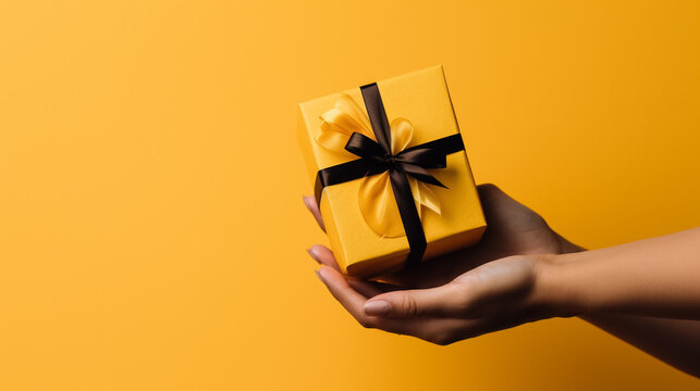 Female hands holding Christmas gift box on yellow background.