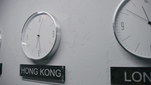 White watches with running time pointers show time zones of different cities. Walking wall clocks in office with modern design. Names of big cities written under clocks. Strict interior. Dolly shot.