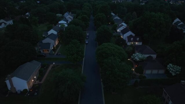 Houses in upscale, wealthy neighborhood at night. Old, developed trees in line suburban development street in summer. Dark aerial establishing shot during dusk.