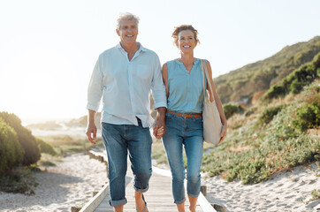 Senior, couple and walking at the beach with hands in portrait for happiness on a vacation in the outdoor. Mature, woman and man holding by ocean for travel on holiday with sunshine for the weekend. - Powered by Adobe