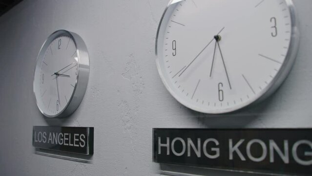 White watches with running time pointers show time zones of different cities. Walking wall clocks in office with modern design. Names of big cities written under clocks. Strict interior. Dolly shot.
