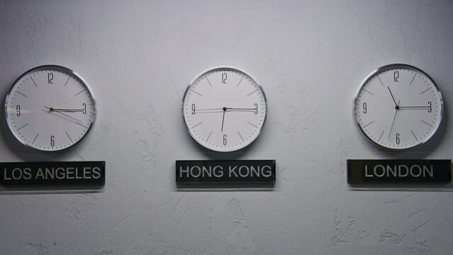 Static shot of walking wall clocks in office with modern design. White watches with running time pointers show time zones of different cities. Names of big cities written under clocks. Time lapse.