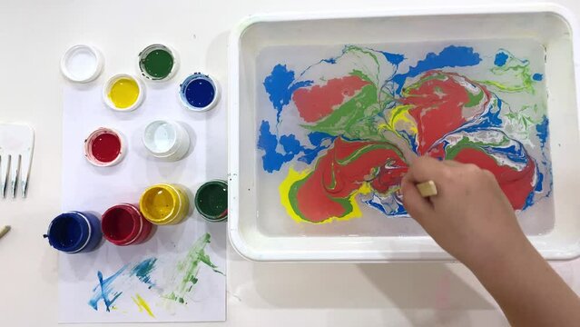 preschooler kid painting with paints on the water top view , Ebru art, creative art for kids. Hobby and relaxing concept.