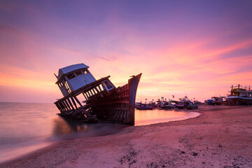 Shooting in long exposure of old shipwreck boat abandoned stand on beach with beautiful sunset at...