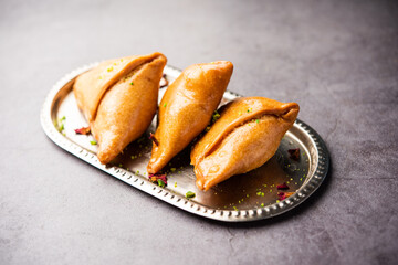 Indian sweet samosa is a Fried pastry soaked in sugar syrup filled with coconut, nuts and fruits