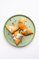 Indian sweet samosa is a Fried pastry soaked in sugar syrup filled with coconut, nuts and fruits