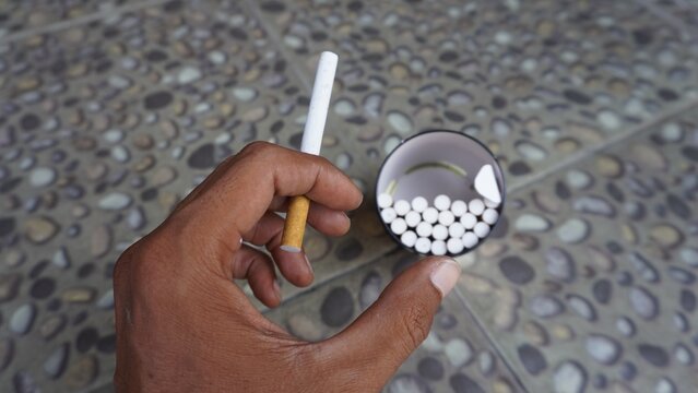 Close up isolated flat lay hand holding cigarette with can full of several cigarettes background. Selective focus