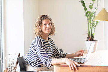 young woman sitting on a table in home office with laptop