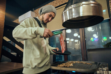 Asian woman cooks meat into the skillet on the stove in the reas