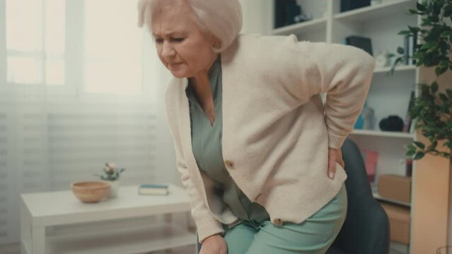 Elderly woman having sharp back pain while getting up, rubbing radiculitis waist