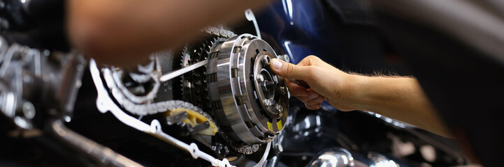 Mechanic repairs motor and chain of motorcycle in workshop. Motorcycle engine repair diagnostics concept