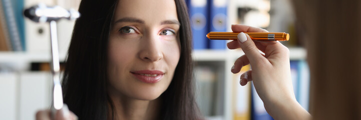 Doctor tests reflexes of eyes of young woman with lamp in medical clinic. Neurological physical...
