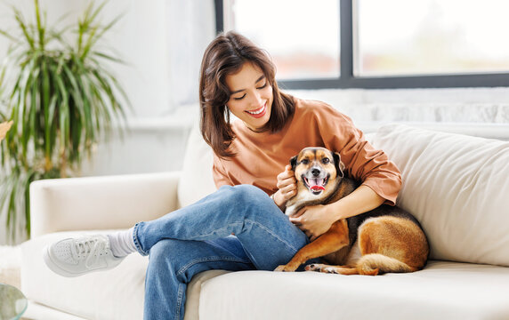 cheerful woman hugging her beloved pet dog at home on the couch.
