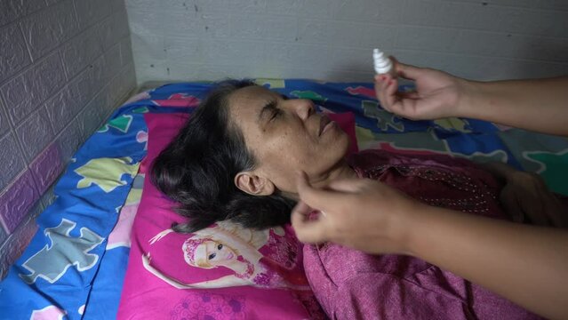 Daughter in law helps put liquid drops in both eyes of old mother in law who is blind with cataracts and has mental illness