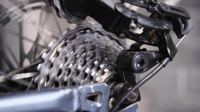 Close-up of a rotating bicycle cassette, chain and gear lever. The chain moves over the gears from large to small. Bicycle workshop. Slow motion