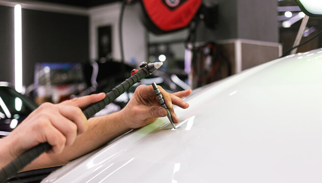 A specialist repairs a dent on the car body without painting. PDR. Process of paintless dent repair on car body. The mechanic at the auto shop with tools to repair dents in car body. Body repair.