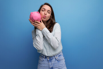 cute 20s brunette lady in shirt and jeans saved up her money for a dream in a piggy bank