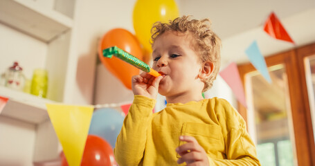 Low Angle Portrait of a Male Kid Using a Party Blower in a Living Room Decorated by Balloons....