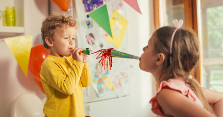Portrait of Two Little Kids Making Noises with Party Horns on Birthday, Surrounded by Colourful...