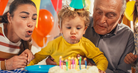 Portrait of a Happy Family Celebrating a Cute Little Boy's Birthday: Mother and Grandfather Help a Child to Blow out his Cake Candles as He Happily Makes a Wish. Memories of Childhood Concept