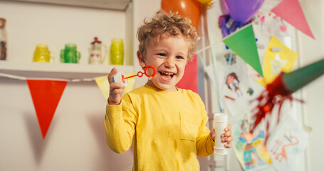 Portrait of a Cute kid in a Yellow Shirt Blowing Bubbles from a Bottle and Laughing. Little Male Toddler Adding Joy and Innocence to the Colorful Atmosphere of a Birthday Party