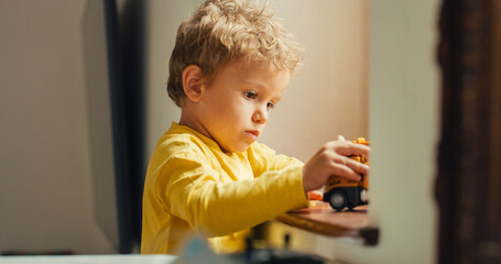 Portrait of a Cute Male Toddler Playing by the Window with Toy Trucks Alone. Little Kid Dreaming of being a Firefighter While Playing with his Toy. Sunny Warm Atmosphere 