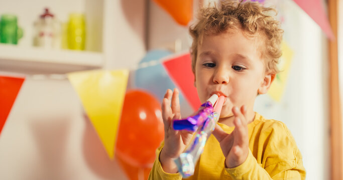 Colorful Happy Atmosphere:  Portrait of Little Cute Boy Blowing Two Party Whistles on his Birthday. Blond Male Toddler Being Playful and making Noise. Concept of Innocence, Fun and Childhood 