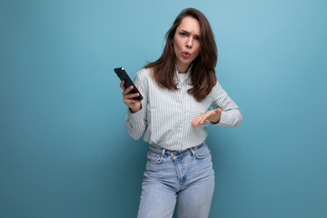 25 year old brunette woman uses a smartphone in her hand on a blue background with copy space