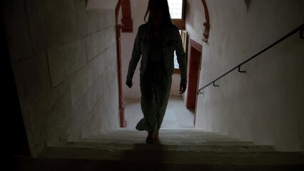 Woman walking up the stairs in a dark hallway.