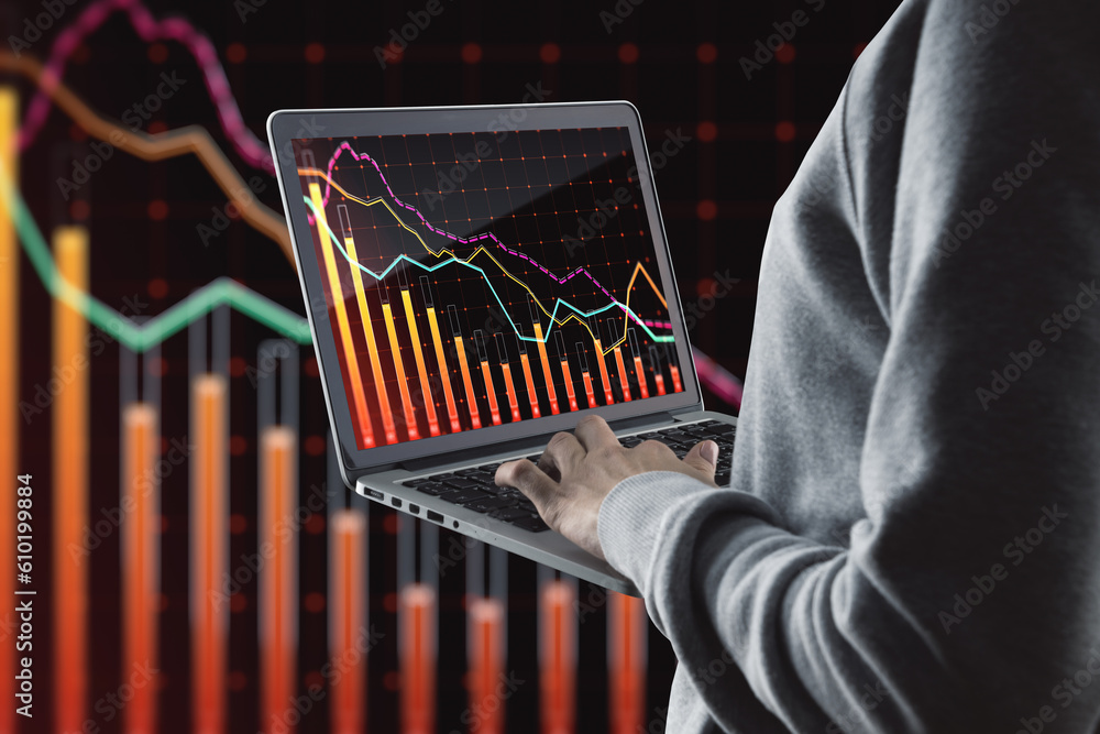 Poster close up of hand holding and using laptop with downward red crisis chart grid on blurry dark backgro