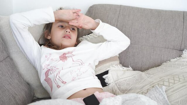 Portrait of 8 years girl in pajamas lying on sofa at home and watching TV. High quality 4k footage