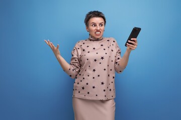 indignant young caucasian dark-haired lady in skirt and blouse with short haircut holding smartphone