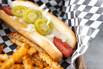 A closeup view of a hot dog, featuring onions and jalapenos.