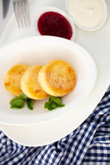 Round cottage cheese pancakes in a white plate on a blue background. Food breakfast. Healthy food. Sour cream sauce and mint. Top view closeup. Dessert meal. Curd cheese pancake ricotta fritters.
