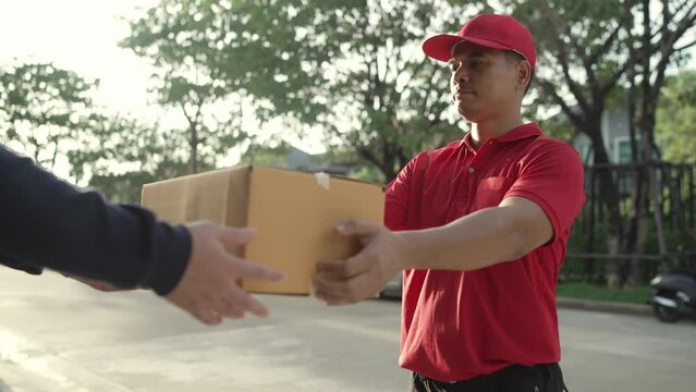 A parcel delivery worker wearing a red uniform is holding a parcel box to the recipient. contact the receiver in front of the house