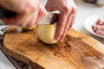 Fototapeta na wymiar A man cuts onions on a wooden board with a sharp knife