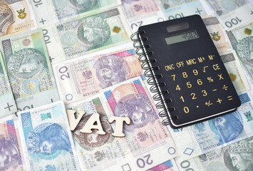 Napis VAT, kalkulator, a w tle rozne banknoty, zlotowki o roznych nominalach.
