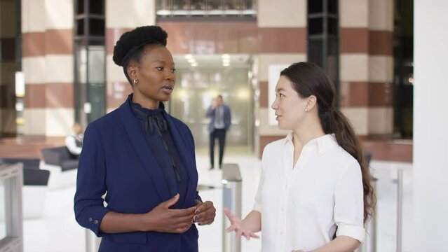 Portrait of two female professionals in conversation before turning to camera and smiling