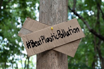 Cardboard from boxes cover with texts '#BeatPlasticPollution', 2023 world environment day motto, was sticked on tree bark to call out all people to care about and to beat the pollution from plastic.