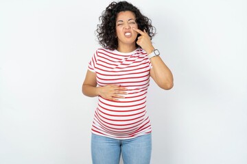 young pregnant woman wearing striped t-shirt over white background pointing unhappy to pimple on...