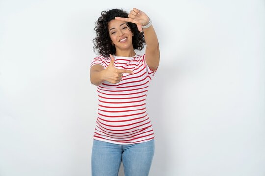 young pregnant woman wearing striped t-shirt over white background making finger frame with hands. Creativity and photography concept.