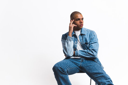 Black Guy In Denim Clothing Sitting On A Chair Isolated Against A White Background. High-quality Photo