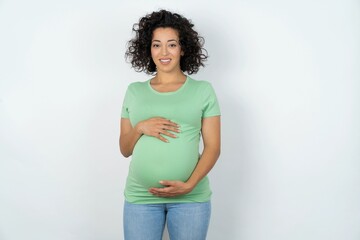 young pregnant woman wearing green t-shirt over white background with nice beaming smile pleased expression. Positive emotions concept